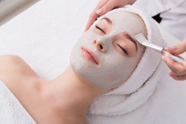 Face peeling mask, spa beauty treatment, skincare. Woman getting facial care by beautician at spa salon, side view.