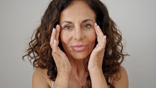 Woman smiling while applying skin treatment.